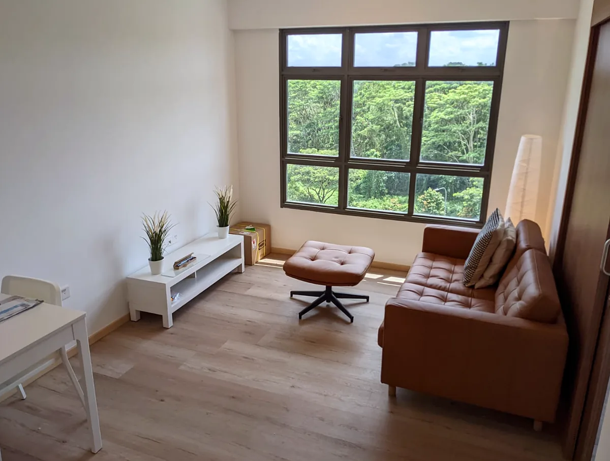 Living room with a tan leather sofa, wood-look vinyl flooring and a window looking out to greenery